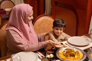 مائدة طعام مليئة بالوجبات الرمضانية المتنوعة، الأعياد والمناسبات الاسلامية، نقاشات وحوارات عائلية، أجواء أسرية مليئة بالحب، اجتماع الاسرة حول مائدة الطعام ، ام عربيه خليجيه اماراتيةترتدي العباءة و الحجاب تقوم بتناول الافطار برفقة ابنها ، المأكولات والمقبلات الشهية ، شهر الخير والبركة