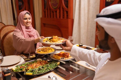 المناسبات الاسلامية و الدينية، ايماءات السعادة و السرور، مائدة إفطار رمضانية مع أصناف مختلفة من الأطعمة الإماراتية الشهية،امراه عربيه خليجيه اماراتية ترتدي العباءة و الحجاب تجلس على الطاولة تقوم بتناول الافطار مع زوجها