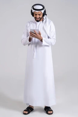 Responding to inquiries and questions, the concept of customer service, gestures of happiness and joy, monitoring and developing work, recording and documenting notes and complaints, a portrait of an Emirati Gulf Arab employee wearing a kandura and ghutrah, wearing headphones on their head, writing on papers, full-body, white background.