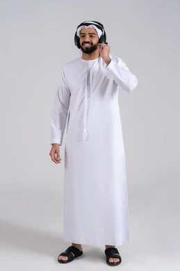 دعم العملاء عبر التواصل لحل المشكلات، الإجابة على الأسئلة والاستفسارات، دمج التقنيات المتطورة مع العمل, النظر الى الكاميرا بتعابيرالسعادة و السرور, بورتريه لشاب عربي خليجي اماراتي يرتدي الكندورة و الغتره يضع الهيدفون، الجسم بالطول الكامل، خلفية بيضاء