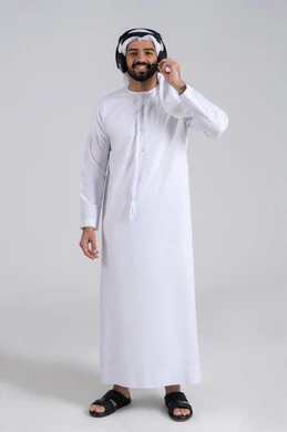 Solving customer issues through direct communication, answering questions and inquiries, integrating advanced technologies with work, looking at the camera with expressions of happiness and joy, a portrait of a young Arab Gulf Emirati man wearing a kandura and ghutrah, wearing headphones, working in the customer service department, with a white background.