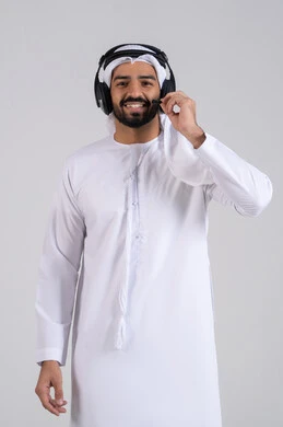 Answering questions and inquiries, integrating advanced technologies with work, looking at the camera with expressions of happiness and joy, a portrait of a young Arab Gulf Emirati man wearing a kandura and ghutrah, wearing headphones, working in the customer service department, communicating with customers to solve problems, white background.