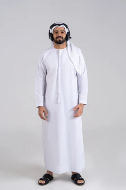 Integrating advanced technologies with work, looking at the camera with expressions of self-confidence, responding to inquiries and questions, a portrait of a young Arab Gulf Emirati man wearing a kandura and ghutrah, wearing headphones, working in the customer service department, communicating with customers to solve problems, full-body image, white background.