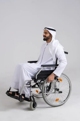 توفير الرعاية والخدمات لأصحاب الهمم، تسهيل الحركة والتنقل عبر الأجهزة والمعدات، شعور المعاقين بالإنتماء والتقدير والإحترام في الامارات العربيه، بورتريه من الجانب لرجل عربي اماراتي خليجي من ذوي الاحتياجات الخاصه يجلس على كرسي متحرك، خلفيه بيضاء