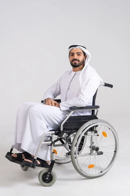 Devices and equipment to facilitate daily mobility, looking at the camera with gestures of happiness and joy, improving the lives of people with physical disabilities, a portrait of an Arab Gulf Emirati man with special needs wearing a kandura and a white ghutrah sitting in a wheelchair, white background.