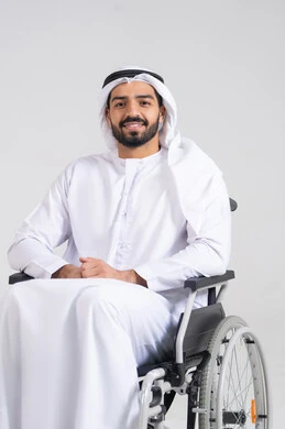 تحسين حياة ذوي الاعاقه الحركيه، توفير اجهزة ومعدات تساعد بالحركة والتنقل، بورترية لرجل عربي خليجي اماراتي من ذوى الاحتياجات الخاصة يرتدي الكندورة و الغترة البيضاء يجلس على كرسي متحرك، النظرالى الكاميرا بايماءات السعادة و السرور ، خلفيه بيضاء