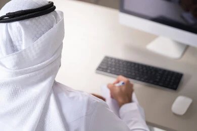 Saving notes and documenting complaints, daily planning and time management, task management and organizing work, a picture from behind of a young Arab Gulf Emirati man wearing traditional attire writing daily goals.