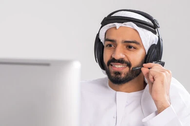 التواصل مع الزبائن لحل المشكلات والشكاوي، الإجابة والرد على الاستفسارات والاستعلامات, استخدام سماعات الرأس والتقنيات المتطورة في العمل, صورة مقربة لشاب عربي خليجي اماراتي يرتدي الكندورة و الغتره يضع الهيدفون يعمل في قسم خدمة العملاء