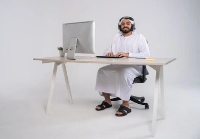 Office professions and jobs, inquiries and communication department, answering questions and inquiries, concept of customer service, an Emirati Gulf Arab employee wearing a kandura and ghutrah and headphones working on a computer in the office, integrating work with technology and technology, managing and organizing the company's work, typing on the keyboard.