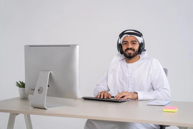 قسم الاستعلامات والاتصال، الإجابة على الأسئلة والاستفسارات، مفهوم خدمة العملاء، موظف عربي خليجي اماراتي يرتدي الكندورة و الغتره و سماعات الرأس يعمل على الحاسوب في المكتب, مهن ووظائف مكتبية , دمج العمل مع التقنية والتكنولوجيا, إدارة وتنظيم أعمال الشركة، النقر على لوحة المفاتيح