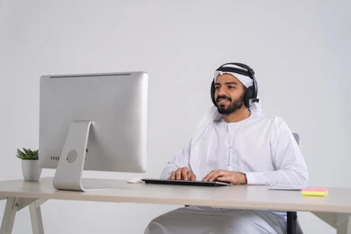 مفهوم خدمة العملاء، الإجابة على الأسئلة والاستفسارات, قسم الاستعلامات والاتصال، موظف عربي خليجي اماراتي يرتدي الكندورة و الغتره و سماعات الرأس يعمل على الحاسوب في المكتب, مهن ووظائف مكتبية , دمج العمل مع التقنية والتكنولوجيا, إدارة وتنظيم أعمال الشركة، النقر على لوحة المفاتيح