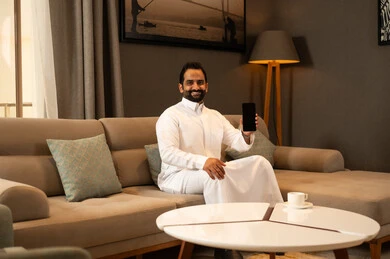 A black screen displayed on the mobile phone, gestures of happiness and joy, browsing the internet via the mobile phone, a Saudi Arabian Gulf man wearing a white thobe sitting in the living room. A black screen displayed on the mobile phone, gestures of happiness and joy, browsing the internet via the mobile phone, a Saudi Arabian Gulf man wearing a white thobe sitting in the living room.