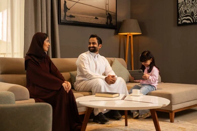 قضاء وقت ممتع مع الابناء، مناقشات و حوارات بين الزوجين، دمج التعلم بالتكنولوجيا، متابعة منصات التعليم الالكتروني عبر الانترنت، فتاة عربية خليجية سعودية ترتدي لباس الكاجوال تجلس فى غرفه المعيشة تستخدم التابلت تجلس برفقة والديها، تعابير السعادة و السرور