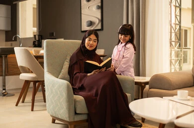 Sharing the reading of useful stories with children, the concept of education based on love and affection, a Gulf Arab Saudi mother reading entertaining novels to her daughter, spending enjoyable time with the daughter, expressions of happiness and joy.