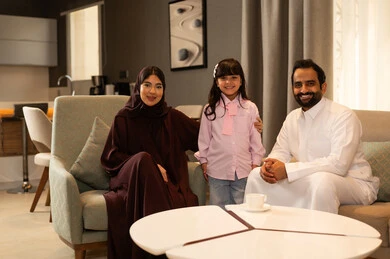 تعزيز المحبة والانسجام داخل الأسرة، رعاية الآباء بأبنائهم والاهتمام بهم، عائلة عربيه خليجيه سعودية ترتدي الزي التقليدي تجلس فى غرفه المعيشة ينظرون للكاميرا بإيماءات السعادة