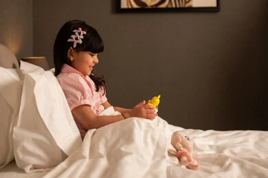 الاستمتاع بالهواية المسلية، ايماءات السعادة و السرور، فتاه عربيه خليجي سعودية ترتدي الزي الكاجوال تجلس على السرير فى غرفه النوم تمسك بيديه لعبه