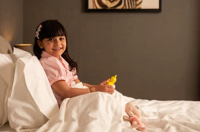 قضاء وقت ممتع بنشاط مسلي، ايماءات السعادة و السرور، فتاه عربيه خليجي سعودية ترتدي الزي الكاجوال تجلس على السرير فى غرفه النوم تمسك بيديه لعبه