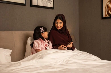 الحب والحنان الاسري، مفهوم الأمومة والطفولة، إجراء مكالمة فيديو، امراة عربيه خليجية سعودية محجبه ترتدي العباءة تجلس فى غرفه النوم برفقة ابنتها تقوم باستخدام الهاتف المحمول، رعاية الأم لأطفالها والعناية بهم ، قضاء أوقات ممتعة مع الابناء