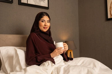 قضاء وقت ممتع و هادئ, الجلوس والاستمتاع بالمشروبات الساخنة والأعشاب الشتوية الدافئة, احتساء المشروب المفضل,  امراه عربيه خليجية سعودية محجبه ترتدي العباءة تجلس على السرير فى غرفه النوم تحمل بيدها فنجان من الشاي، ايماءات السعادة والسرور