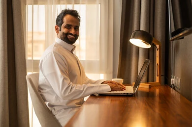 استخدام جهاز تقني حديث لإنجاز المهام والمشاريع، إيماءات التركيز في شاشة الكمبيوتر, تصفح مواقع التواصل الاجتماعي والعمل عن بعد, رجل عربي خليجي سعودي يرتدي الثوب الابيض يجلس على المكتب يستخدم الحاسوب المحمول