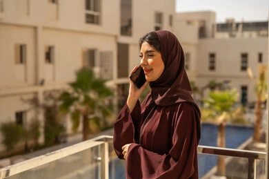 اجراء مكالمة هاتفية عبر الجوال ، قضاء وقت ممتع فى الخارج ، امراه عربيه خليجيه سعودية محجبة ترتدي العباءة تمسك بيديها الهاتف المحمول، النظر بتعابير السعادة و السرور، الدردشة مع الاهل و الاصدقاء