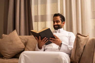 حب المطالعة والقراءة، الاهتمام بتصفح الكتب المفيدة، رجل عربي خليجي سعودي يرتدي الثوب الابيض يجلس على الاريكة فى غرفه المعيشة يمسك بيده كتاب, تنمية وزيادة الذخيرة الفكرية حب المطالعة والقراءة، الاهتمام بتصفح الكتب المفيدة، رجل عربي خليجي سعودي يرتدي الثوب الابيض يجلس على الاريكة فى غرفه المعيشة يمسك بيده كتاب, تنمية وزيادة الذخيرة الفكرية