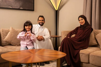 تعابير تدل على الفرح والسعاده لقضاء الوقت مع الاهل،  ايماءات يدين عل شكل قلب، مفهوم الأسره السعوديه السعيده، عائله عربيه خليجيه سعوديه تجلس في غرفه المعيشه الى تنظرالى الكاميرا