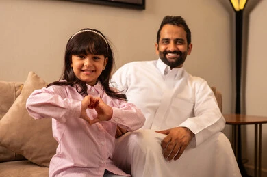 مفهوم الترابط الأسري بين أفراد العائلة، رجل عربي خليجي سعودي يرتدي الملابس التقليديه يجلس مع ابنته فى غرفه المعيشة ، تقوية الروابط والعلاقات مع الأطفال بالعطف و الحنان،  ايماءات يدين عل شكل قلب