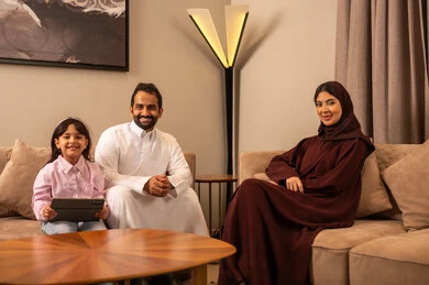 Using a tablet device, the concept of a happy Saudi family, an Arab Gulf Saudi family sitting in the living room looking at the camera, expressions indicating joy and happiness spending time with family.