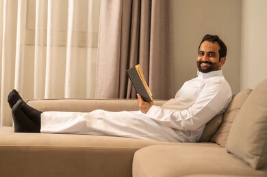 الانسجام و الهدوء و السكينة، ثقافة التعلم الذاتي, الاستمتاع بقراءة كتاب، رجل عربي خليجي سعودي مبتسم يرتدي  الثوب الابيض يمسك بيده كتاب, إيماءات السعادة و السرور, قضاء وقت ممتع