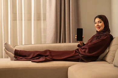 عرض شاشة سوداء فارغه عبر الجوال، امراه عربية خليجية سعودية ترتدي الحجاب والعباءة تنظر تجلس على الأريكة في غرفة المعيشة و تمسك بيديها الهاتف المحمول ، تعابير السعادة و السرور عرض شاشة سوداء فارغه عبر الجوال، امراه عربية خليجية سعودية ترتدي الحجاب والعباءة تنظر تجلس على الأريكة في غرفة المعيشة و تمسك بيديها الهاتف المحمول ، تعابير السعادة و السرور