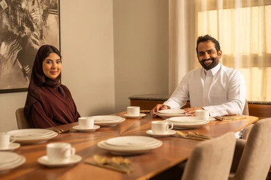 قضاء وقت ممتع، تعابير السعادة و السرور، زوجان عربيان سعوديان خليجيان يرتديان الزي التقليدي يجلسان على مائدة الطعام في المنزل ، اسرة عربية خليجية سعيدة، أجواء عائلية سعيدة, عطلة نهاية الأسبوع