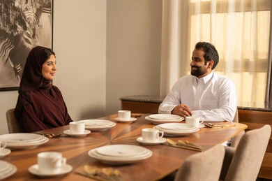 زوجان عربيان سعوديان خليجيان يرتديان الزي التقليدي يجلسان على مائدة الطعام في المنزل ، اسرة عربية خليجية سعيدة، قضاء وقت ممتع، أجواء عائلية سعيدة, عطلة نهاية الأسبوع