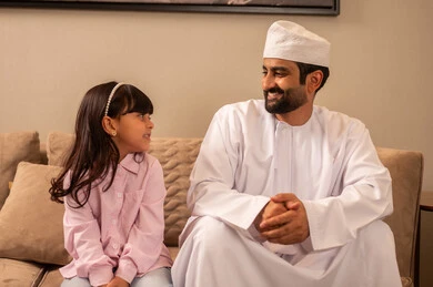 مشاعر الأمان والحب مع العائلة، العناية والاهتمام بالأبناء، مفهوم العاطفة عند الاباء،رجل عربي خليجي عماني يرتدي الدشداشة و الكمة ينظر الى ابنته بإيماءات السرور والفرح، الحنان والعطف على الأولاد