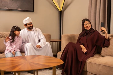 الاجتماع الأسري في غرفة المعيشة، بناء مجتمع سعودي متنامي، فرحة الابنة بقضاء وقت ممتع مع الأهل، التقاط سيلفي عائلي تذكاري عبر الهاتف المحمول, عائلة عربية سعودية خليجية مبتسمة تقوم بتوثيق اللحظات الممتعة بإيماءات السعادة والفرح