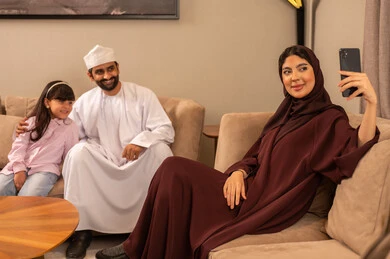 بناء مجتمع سعودي متنامي، الاجتماع الأسري في غرفة المعيشة، فرحة الابنة بقضاء وقت ممتع مع الأهل، التقاط سيلفي عائلي تذكاري عبر الهاتف المحمول, عائلة عربية سعودية خليجية مبتسمة تقوم بتوثيق اللحظات الممتعة بإيماءات السعادة والفرح