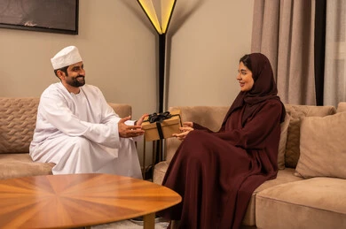 التعبير عن الألفة و المودة بين الزوجين, إيماءات السعادة والسرور, رجل عربي خليجي عماني يرتدي الدشداشة والكمة يقدم لزوجته هديه بمناسبة عيد الحب, الاحتفال بالمناسبات و الأعياد