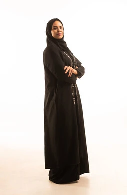 بورتريه لامرأة عربية خليجية سعودية مبتسمة ترتدي العباءة السوداء والحجاب، الوقوف بايدى متقاطعة، ايماءات الفخر والاعتزاز، النظرالى الكاميرا، خلفية بيضاء