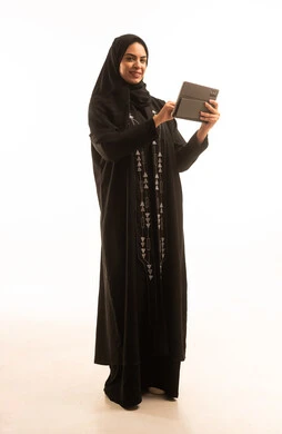 A portrait of a Saudi Arabian Gulf woman wearing a black abaya and a hijab, using a tablet, full-body shot, accomplishing tasks remotely, online shopping, using modern and advanced devices and technologies, with a white background.