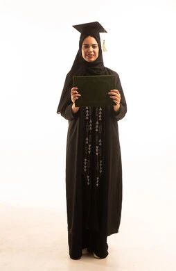 الفرح بتحقيق حلم النجاح ، بورتريه لخريجة عربية خليجية سعودية محجبة ترتديعباءة سوداء والقبعة تحمل بيدها الشهادة، النجاح والتفوق والتخرج من الجامعة، إيماءات السعادة بالوصول الى الحلم، خلفية بيضاء