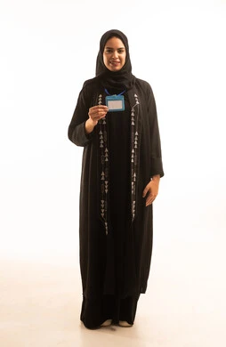 Highlighting personal identity, a portrait of a smiling Saudi Arabian Gulf woman wearing a black abaya and a hijab, holding a blank white card with a blue ribbon and looking at the camera, gestures of self-confidence, white background.