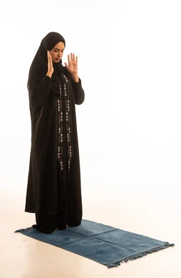 ايماءات تدل على الخشوع في الصلاة، بورتريه لإمرأة عربية خليجية سعودية ترتدي الحجاب والعباءة السوداء تقف على سجادة الصلاة, أداء الفروض على وقتها, خلفية بيضاء