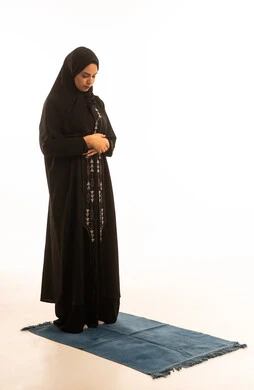 Performance of the Islamic religious obligation, a portrait of a Gulf Arab Saudi woman wearing a hijab and a black abaya standing on a prayer rug, performing the obligatory prayers on time, white background. Performance of the Islamic religious obligation, a portrait of a Gulf Arab Saudi woman wearing a hijab and a black abaya standing on a prayer rug, performing the obligatory prayers on time, white background.