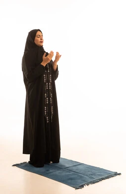 التقرب الى الله من خلال الإجتهاد في العبادة والحفاظ على الصلاه، بورتريه لإمرأة عربية خليجية سعودية ترتدي الحجاب والعباءة السوداء تسجد على سجادة الصلاة, أداء الفروض على وقتها, خلفية بيضاء