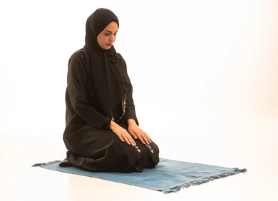 الإجتهاد في الطاعات والأدعية والاذكار،  بورتريه لإمرأة عربية سعودية خليجية محجبة ترتدي عباءة سوداء تجلس على السجادة تقوم بآداء فريضة الصلاة، مفهوم العبادة و التقرب الى رب العالمين، خلفية بيضاء