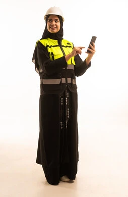 Browsing the internet via phone, a portrait of a Saudi Gulf Arab engineer wearing a jacket and safety helmet monitoring the factory operations using a mobile phone, adopting modern technology and techniques in engineering, studying the fundamentals of the project, full-body, white background.