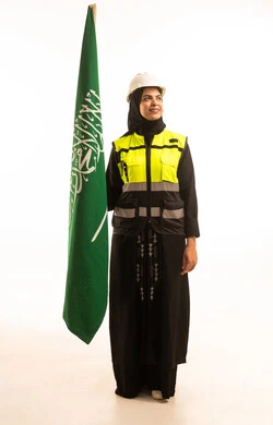Commemorating the Saudi National Day on September 23, a portrait of a Gulf Arab Saudi female engineer wearing a hijab, a helmet, and a safety vest, holding the Kingdom's flag and looking at it with gestures of pride and honor, celebrating Flag Day on March 11, with a white background.
