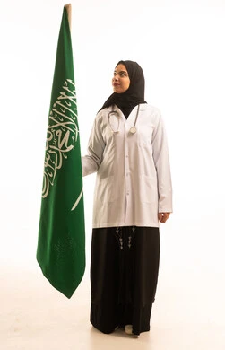 A portrait of an Arab Gulf Saudi female doctor wearing a hijab with a white coat and a stethoscope, commemorating the founding of the first Saudi state on February 22, looking at the flag with gestures of pride, boasting about the country's achievements, with a white background.