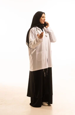 اجراء مكالمة هاتفية عبر الجوال، بورتريه لطبيبة عربية خليجية سعودية ترتدي المعطف الأبيض والسماعة تحمل بيدها هاتف محمول، تقديم الخدمة والاستشارة الطبية، مهن ووظائف نسائية،استخدام التكنولوجيا الحديثة، الجسم بالطول الكامل، خلفية بيضاء