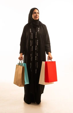 Looking up with gestures of joy and happiness, a portrait of a Saudi Arabian Gulf woman wearing a black abaya and carrying shopping bags, a full-body image, white background.